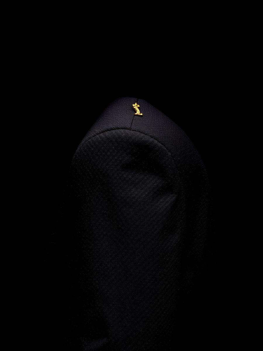 Shoulder detail of a black tailored jacket with a gold thread accent